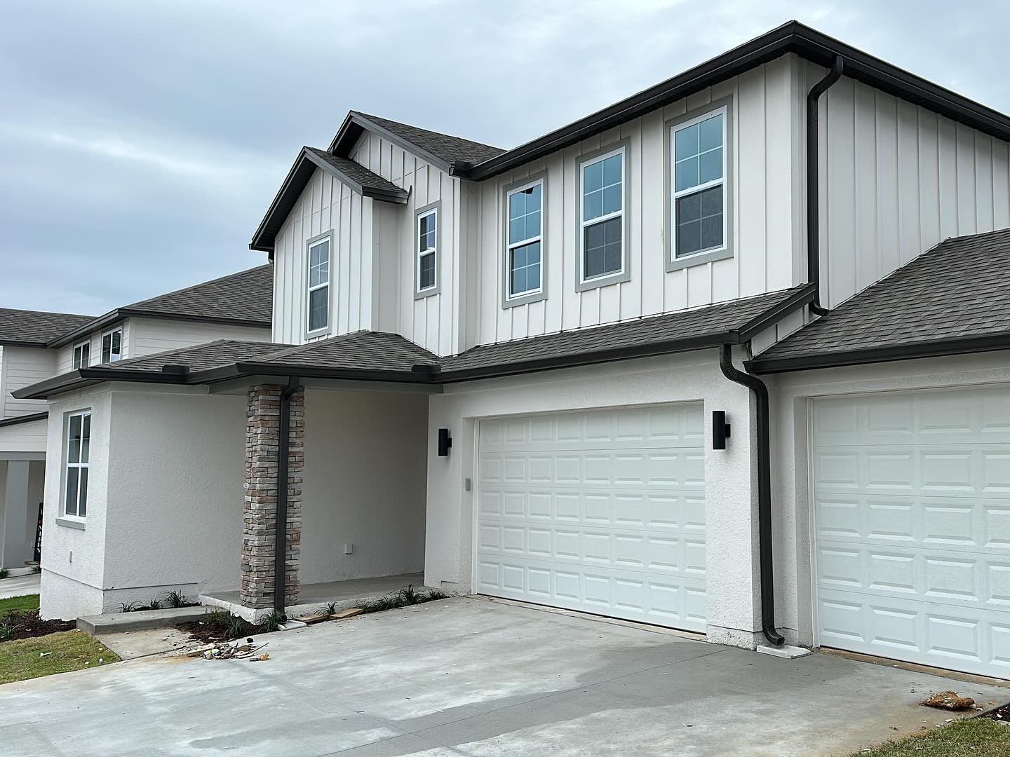 Dark bronze seamless gutters, fascia and downspouts installed on a two-story home with white board-and-batten siding