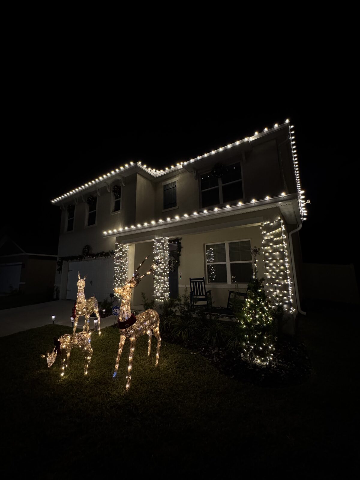 Warm white Christmas lights outlining the roofline and landscaping of a home at night
