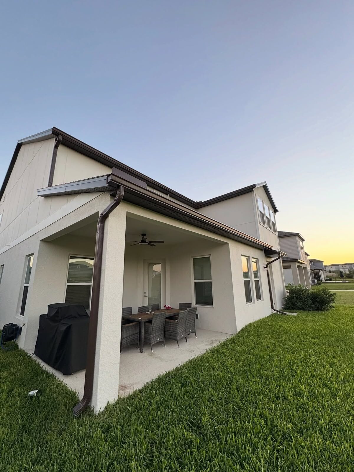 Bronze gutters and downspouts installed around a covered rear patio on a light stucco home