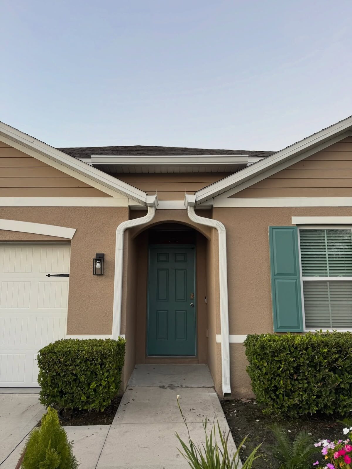 White gutters and downspouts framing the arched front entry of a tan home with green shutters