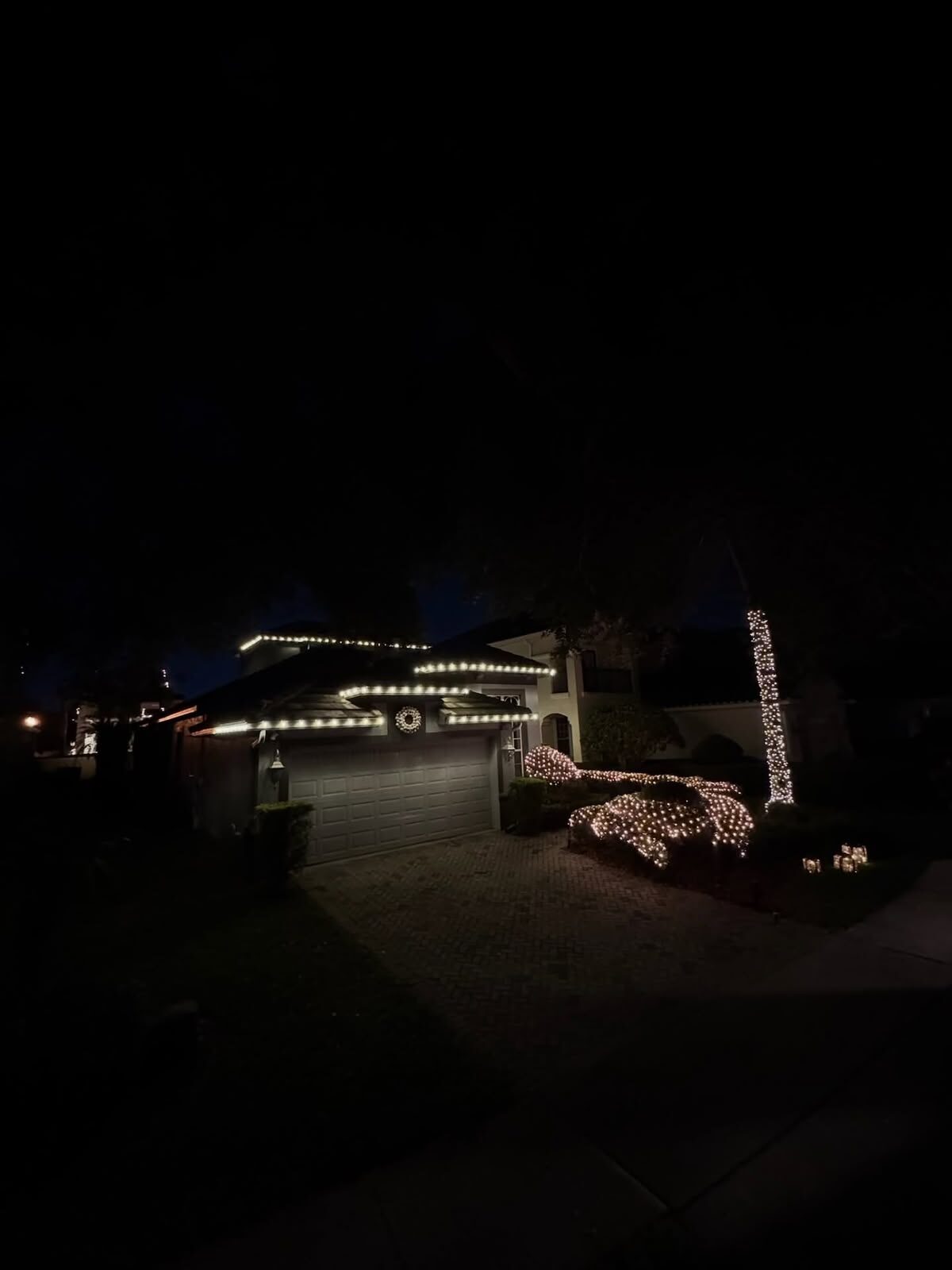 Warm white Christmas lights outlining the roofline, bushes and a column of a home at night