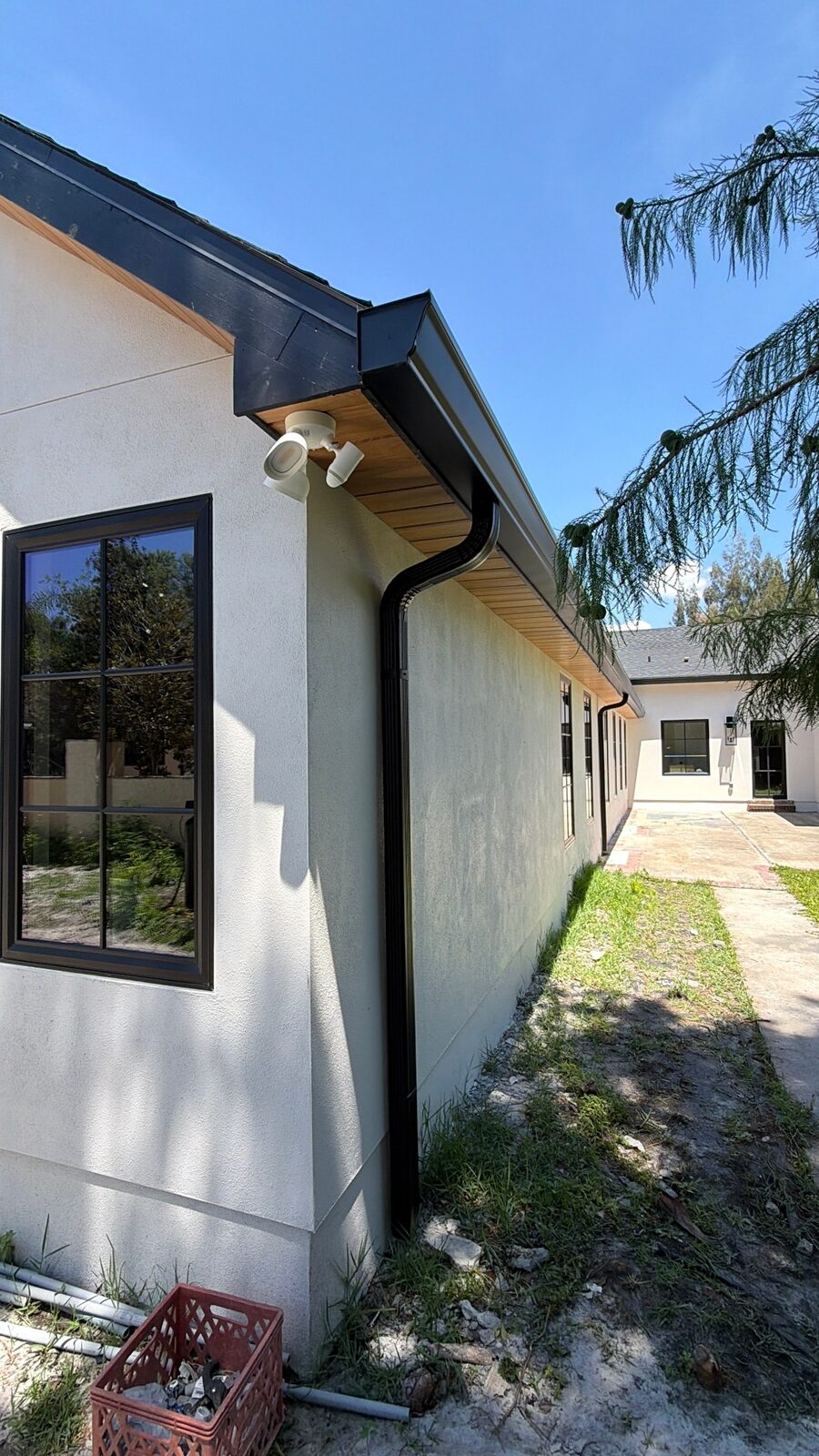 Black seamless gutter and downspout with warm wood soffit running the length of a white stucco home