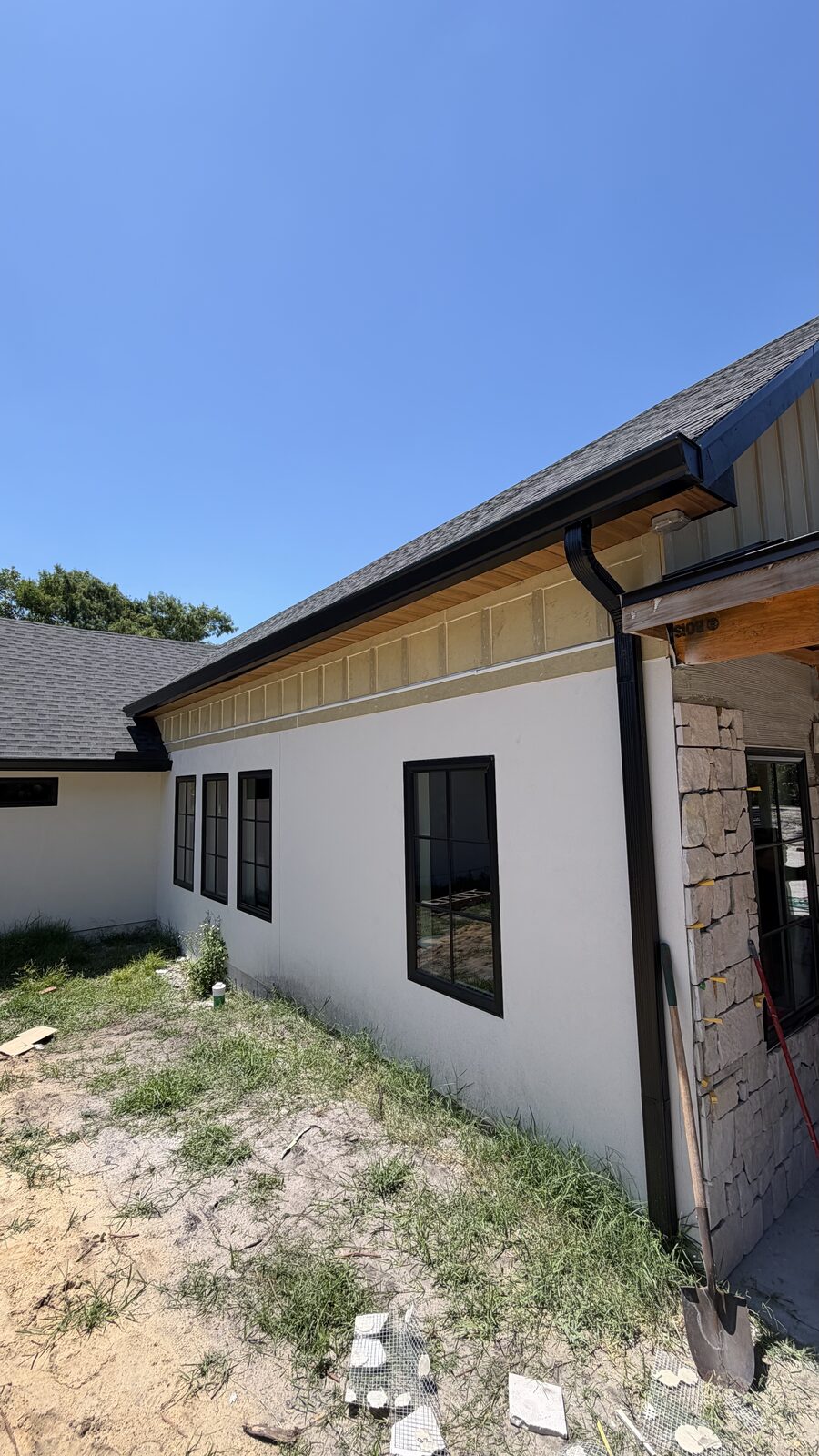 Black seamless gutter and downspout with wood-lined soffit on a white stucco and stone home