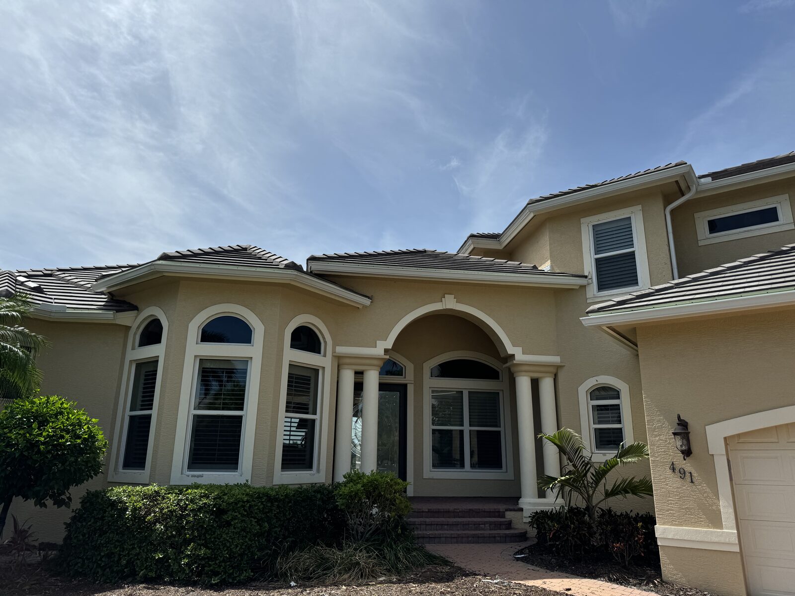 Seamless gutters finished along the tile rooflines of a tan two-story home with an arched columned entry