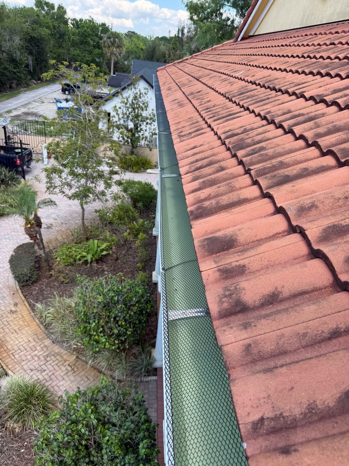Green mesh gutter guard installed over a white gutter beside a barrel tile roof and garden
