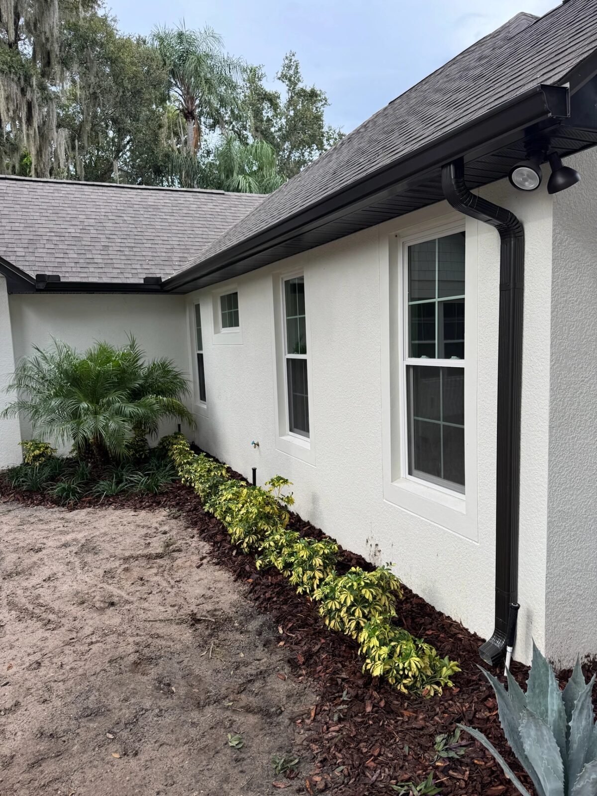 Dark bronze seamless gutters, soffit and downspout installed along the roofline of a white stucco home