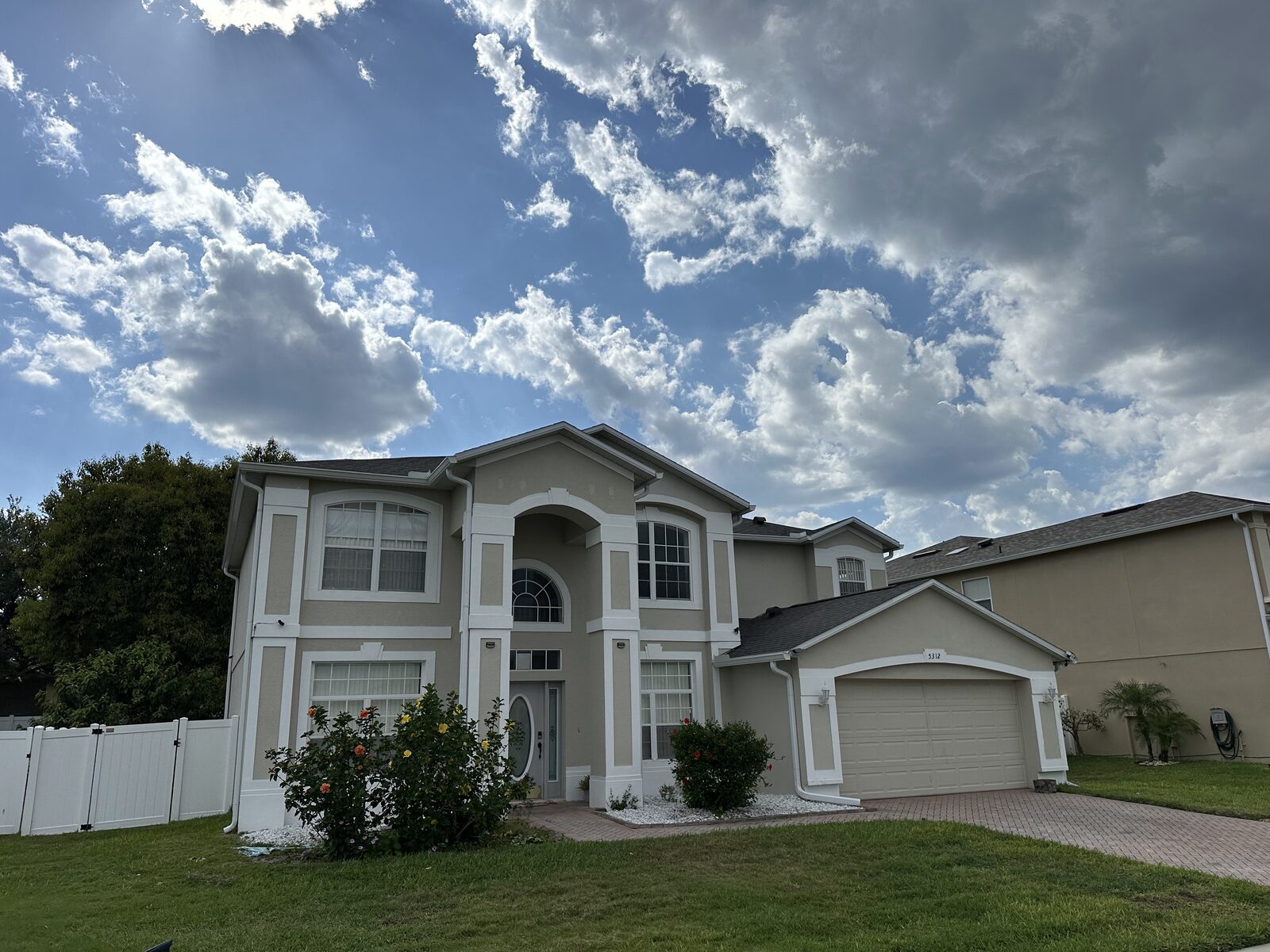 Two-story tan stucco home with white gutters, fascia and downspouts across the full front elevation