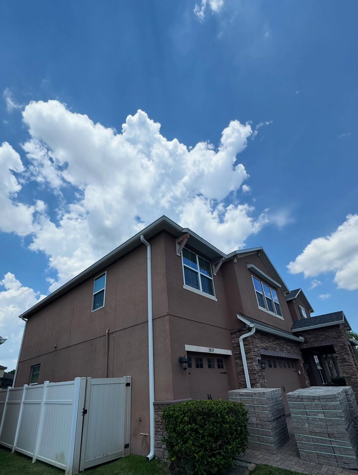 White gutters and a full-height downspout on the side of a two-story stucco home