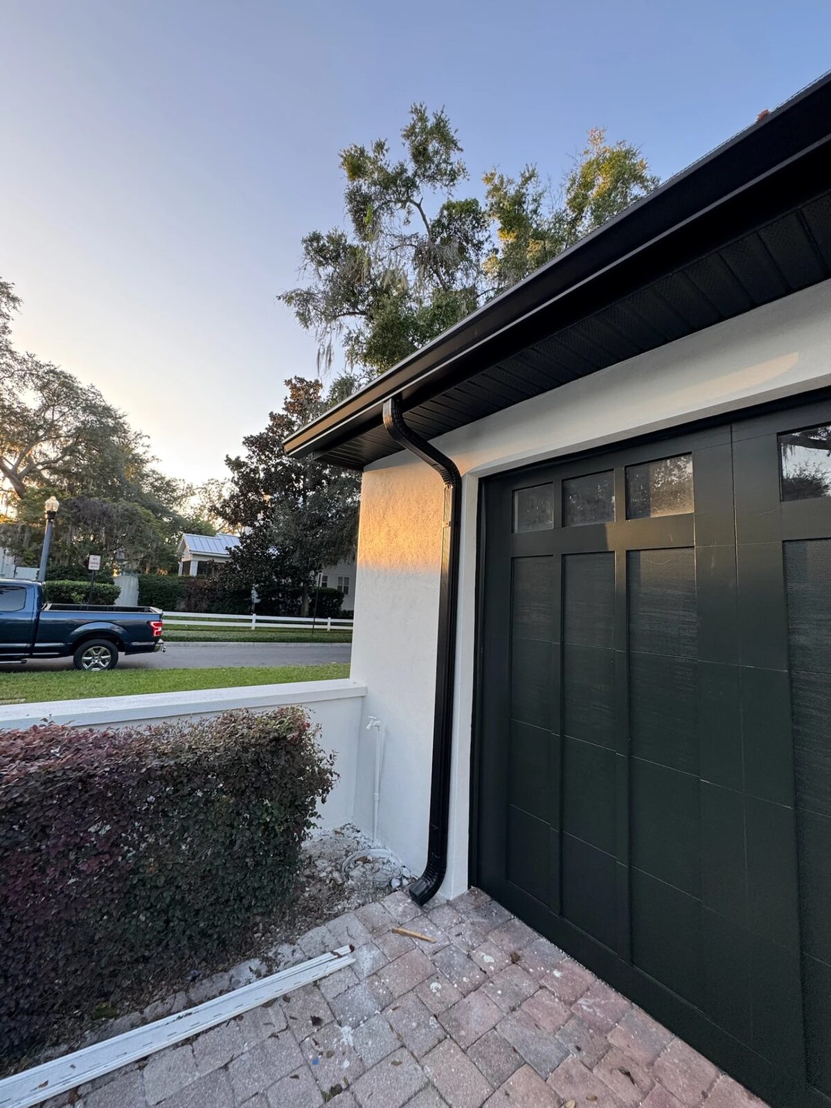 Dark bronze gutter, soffit and downspout installed above a garage door on a white stucco home at sunset