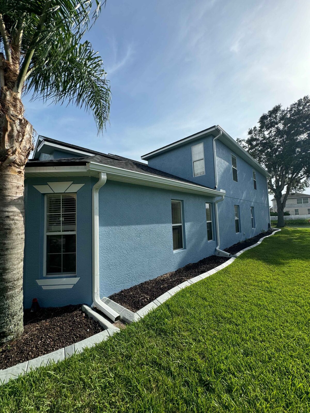 White seamless gutters and downspouts installed along a blue stucco two-story Florida home