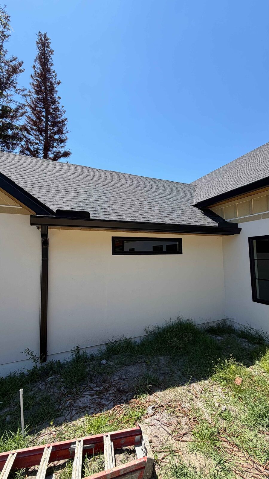 Black seamless gutter and downspout installed on a newly built stucco home with shingle roof