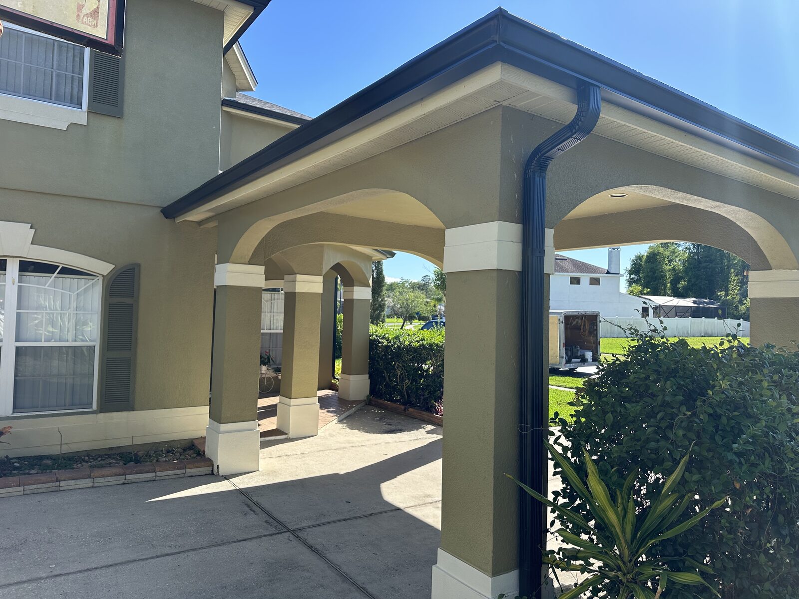 Dark gutter, fascia and downspout installed on a columned covered entry of a stucco home