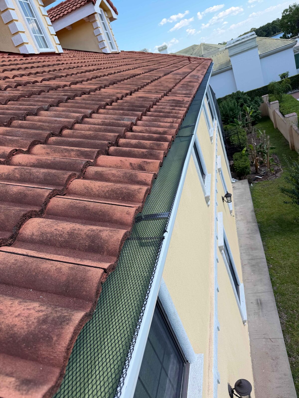 Continuous leaf guard screen along a white gutter on a long barrel tile roofline
