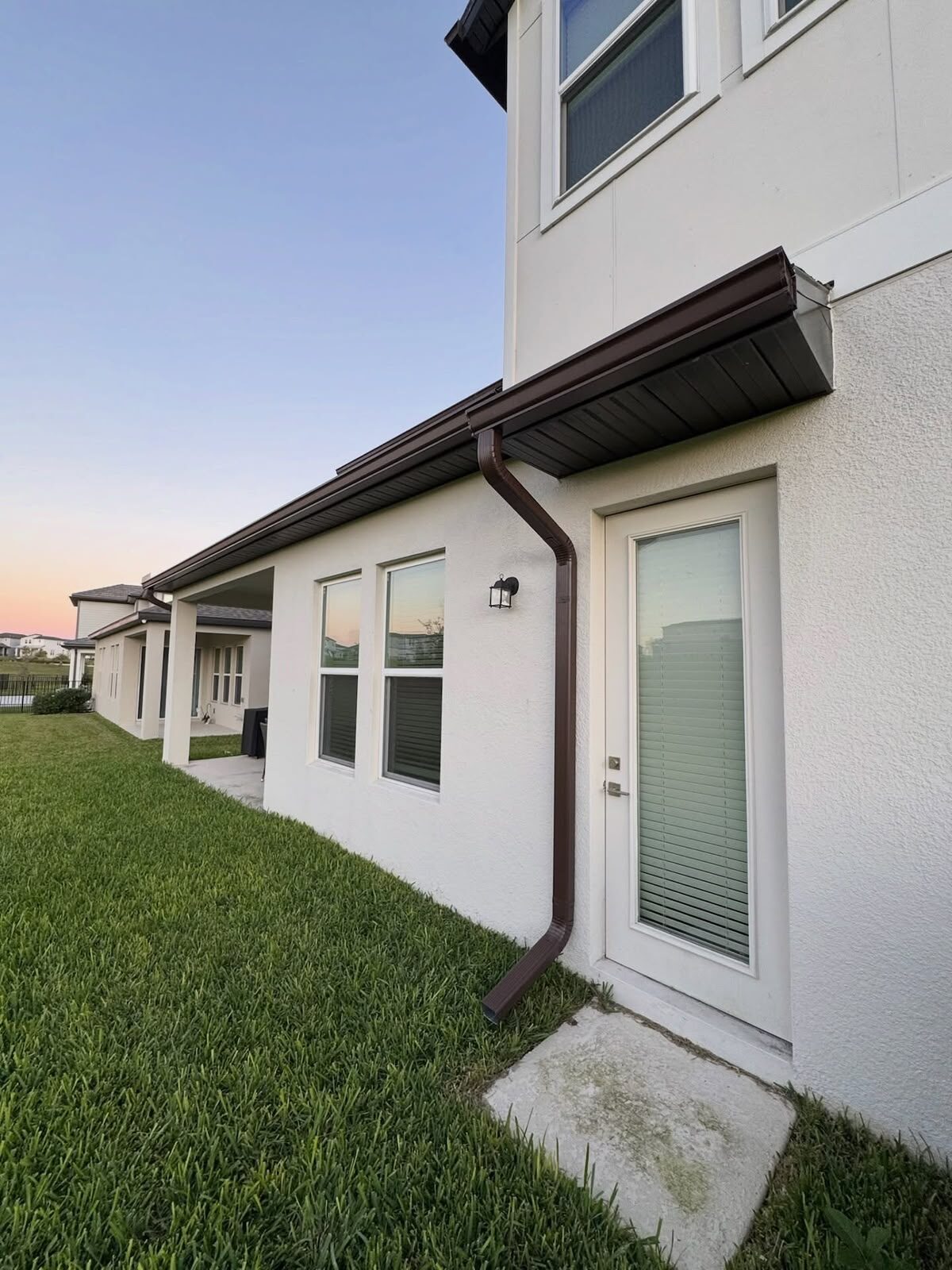 Dark bronze gutter, soffit and downspout running along the eave of a white stucco home at sunset