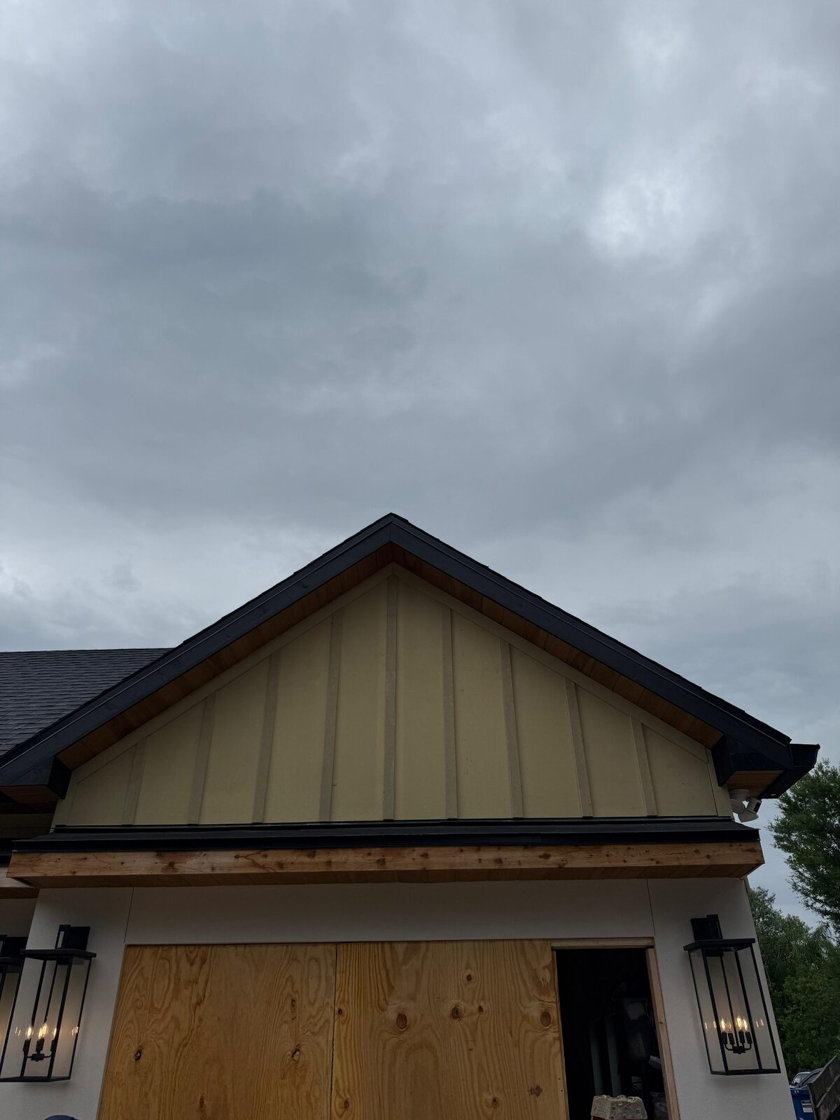 Garage gable with vertical siding, wood soffit and black fascia above a wide garage opening